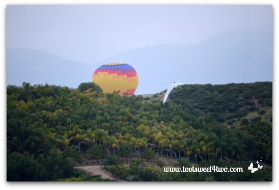 Yellow Center Hot Air Balloon ascending from behind a hill
