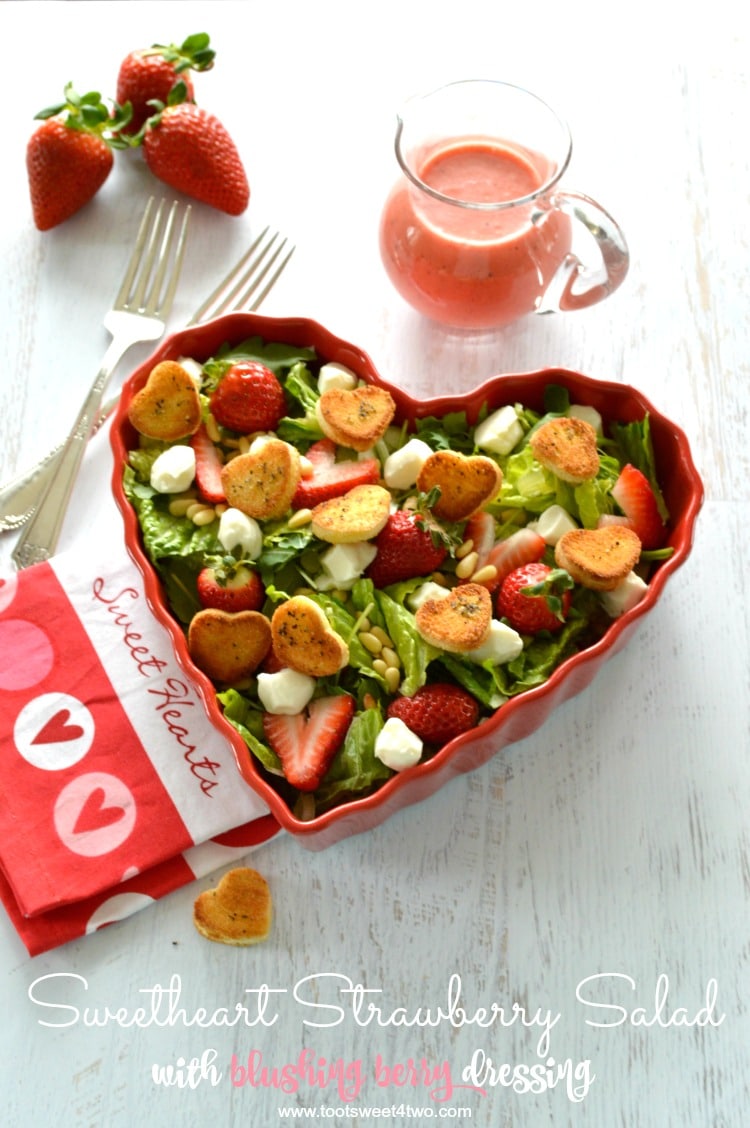 Green salad with strawberries in heart-shaped bowl with mini heart croutons and pink dressing.
