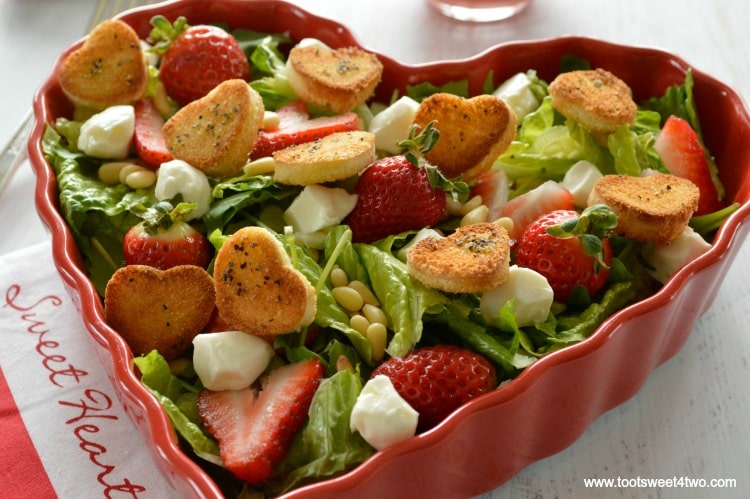 Green salad with strawberries in heart-shaped bowl with mini heart croutons and pink dressing