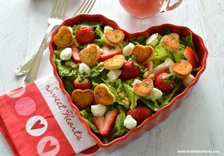 Green salad with strawberries in heart-shaped bowl with mini croutons and pink dressing.